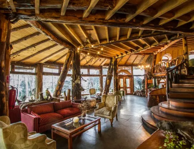 Interior de madera con vigas a la vista, ventanales, sillones y una escalera