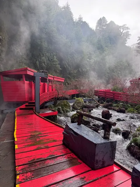 Pasarela roja junto a un curso de agua con rocas cubiertas de musgo