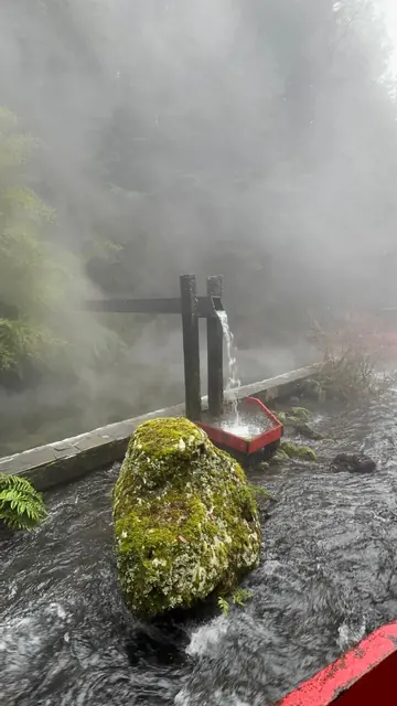 Caída de agua desde una estructura de madera junto a una roca con musgo y vapor