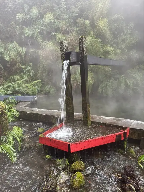 Chorro de agua desde una estructura de madera sobre un borde rojo junto al bosque