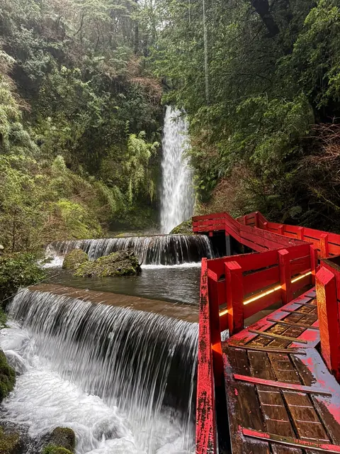Cascada y pequeños desniveles de agua junto a una pasarela roja entre vegetación