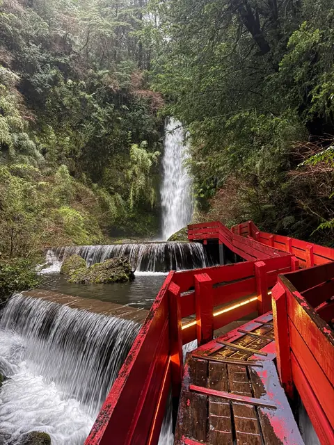 Vista de una cascada y un salto escalonado junto a barandas rojas y bosque