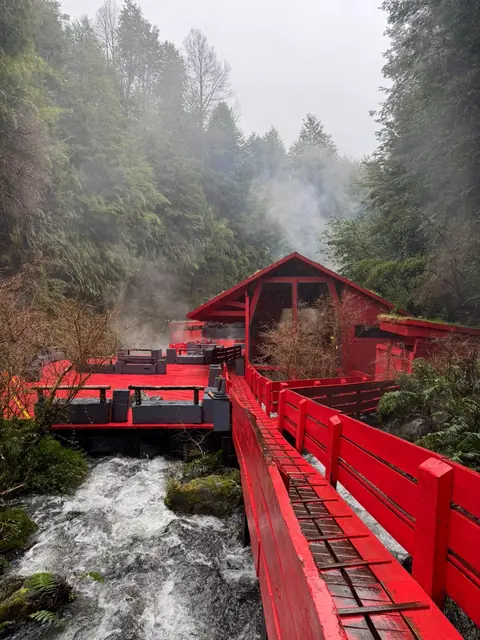 Pasarela roja que conduce a una construcción de madera en una quebrada arbolada