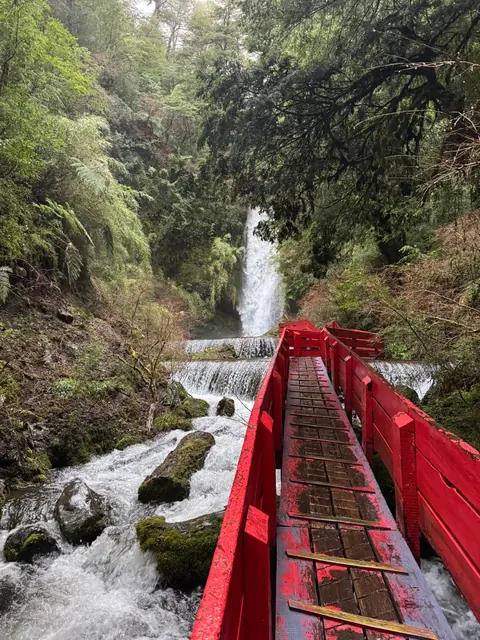 Pasarela roja hacia una cascada entre grandes rocas cubiertas de musgo