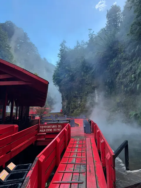 Pasarela y barandas rojas junto a una piscina bajo cielo azul y vapor