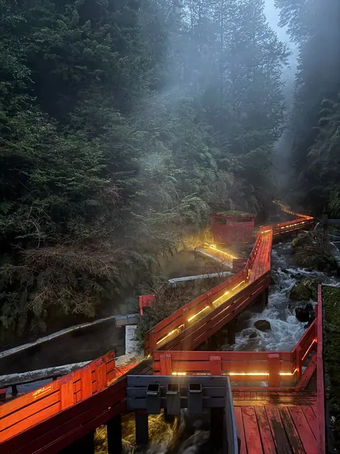 Barandas rojas y luces cálidas sobre el agua en una quebrada al anochecer