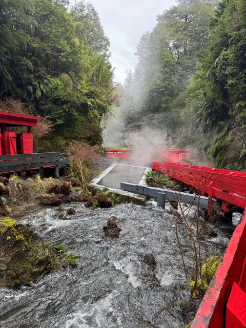 Pasarelas y construcciones rojas junto al agua y vapor en una quebrada boscosa