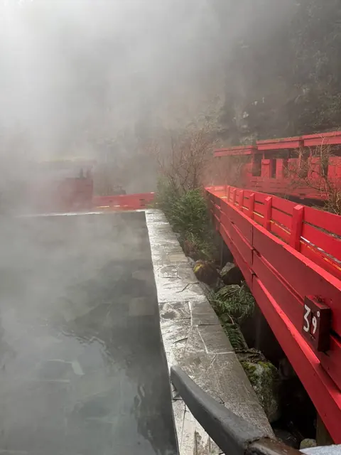 Piscina, borde de piedra y pasarelas rojas rodeados de vapor